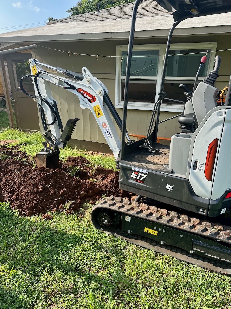 Compact Bobcat excavator digging a garden bed beside a house, bucket resting in fresh soil